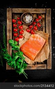 Salted salmon with parsley and tomatoes on a wooden tray. On a black background. High quality photo. Salted salmon with parsley and tomatoes on a wooden tray.
