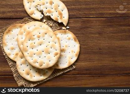 Saltine or soda crackers, photographed overhead on dark wood with natural ight