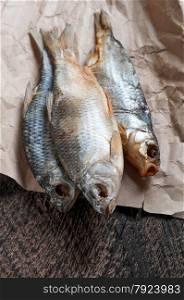Salty dry river fish is on crumpled yellow paper on a brown wooden background