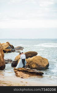 same couple with a bride in a blue dress walk along the ocean shore