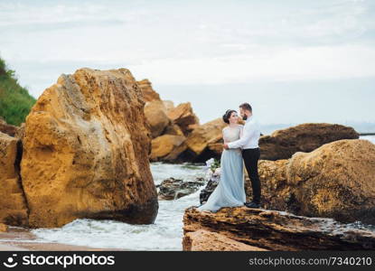 same couple with a bride in a blue dress walk along the ocean shore