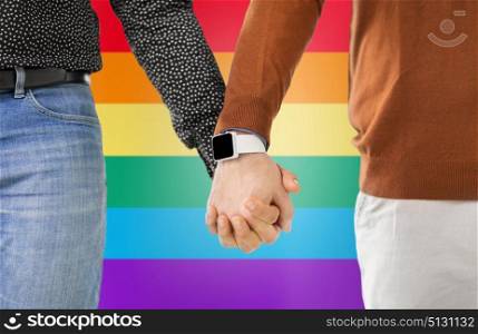 same-sex relationships, lgbt and technology concept - close up of male gay couple holding hands with smartwatch over rainbow colors background. close up of male gay couple hands with smartwatch. close up of male gay couple hands with smartwatch