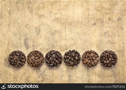sampler of coffee beans from different parts of the world - overhead view of round bowls against handmade textured paper with a copy space