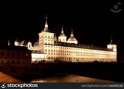 San Lorenzo de El Escorial Monastery at night beautifully illuminated. Four towers are set off by black background.