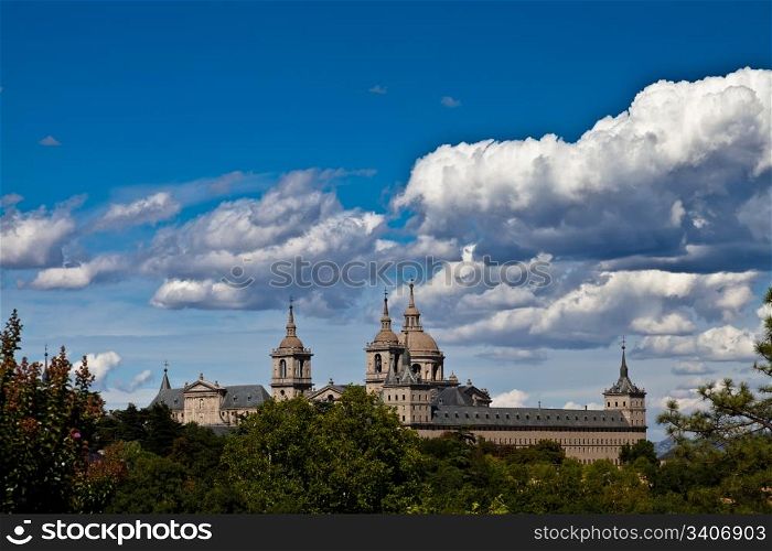 San Lorenzo de El Escorial Monastery from Casita del Infante. The towers of the church and monastery are set of by a bright blue sky.