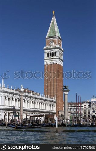 San Marco (St Mark's Square) in Venice in northern Italy. The Campanile, the clock tower and the Biblioteca Marciana (Library of St Mark), with gondolas on the waterfront to the lagoon.