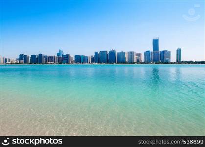 Sand beach blue sea with Abu Dhabi skyline and modern buildings cityscape view from marina island