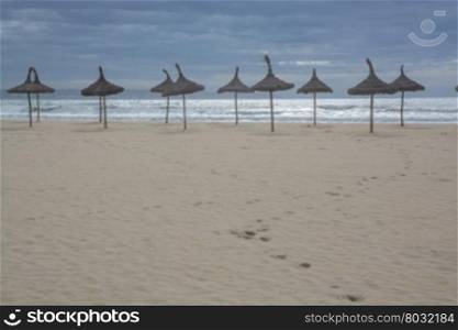 Sand beach with footpath down to the water edge and decorative straw parasols in a straight row.