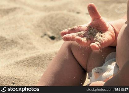 Sand in baby hands. Child playing with beach sand. He has for the first time golden grains of sand in his hands. Infant boy is delight because of learning and discover world with satisfaction and joy.