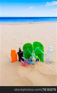 sandals and bottle of water and suntan creams on sandy beach by sea side