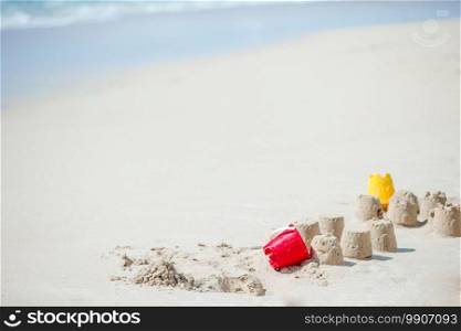 Sandcastle at white tropical beach with plastic kids toys. Bright kid toys on tropical sand beach