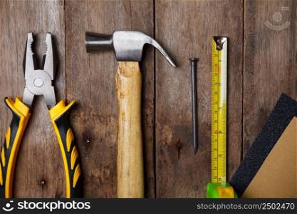 Sandpaper, pliers, measuring tape, hammer and nail on wooden table