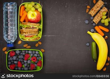 Sandwich, apple, grape, carrot, berry in plastic lunch box and bottle of water on black chalkboard. Back to school concept.