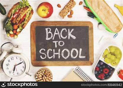 Sandwich, apple, grape, carrot, berry in plastic lunch boxes, stationery and bottle of water on white background. Back to school concept.