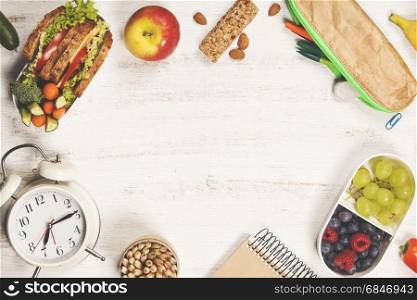 Sandwich, apple, grape, carrot, berry in plastic lunch boxes, stationery and bottle of water on white background. Back to school concept.