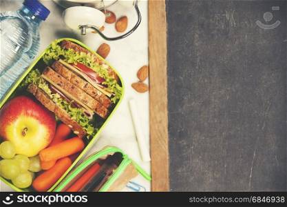 Sandwich, apple, grape, carrot, stationery and bottle of water on white wooden background. Back to school concept.