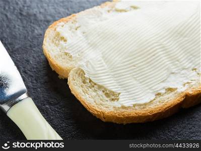 Sandwich, bread with butter and a knife on dark stone background