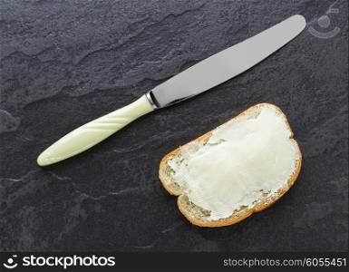Sandwich, bread with butter and a knife on dark stone background