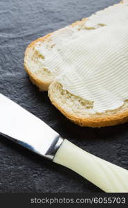 Sandwich, bread with butter and a knife on dark stone background