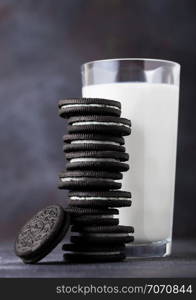 Sandwich cookie consisting of two chocolate wafers with cream filling with glass of milk on stone board.