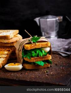 sandwich of French toast and lettuce leaves and boiled egg, a vegetarian food wrapped in paper on a brown wooden board. sandwich of French toast and lettuce leaves and boiled egg