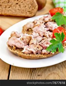 Sandwich of rye bread, brains, tomato and parsley on an oval plate on a wooden boards background