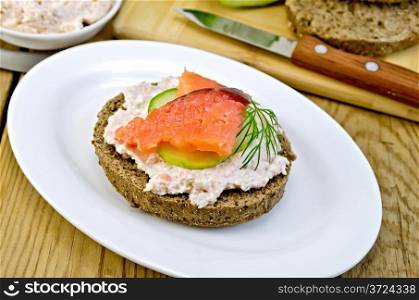 Sandwich of rye bread with cream, cucumber, dill and salmon on a plate on a wooden board