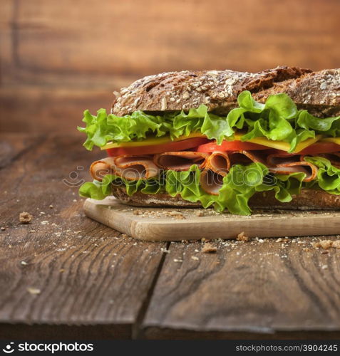 Sandwich on the wooden table with slices of fresh tomatoes, ham, cheese and lettuce
