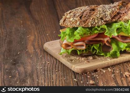 Sandwich on the wooden table with slices of fresh tomatoes, ham, cheese and lettuce