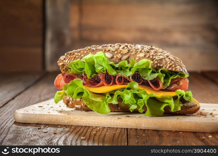 Sandwich on the wooden table with slices of fresh tomatoes, ham, cheese and lettuce