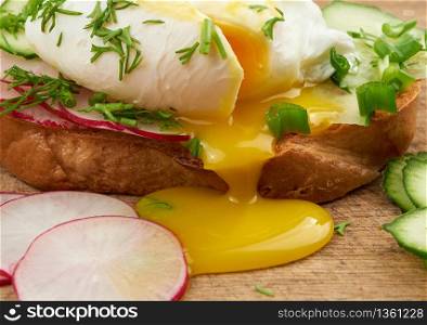 sandwich on toasted white slice of bread with poached eggs, dill and with slices of green onions, yellow yolk flows from the egg