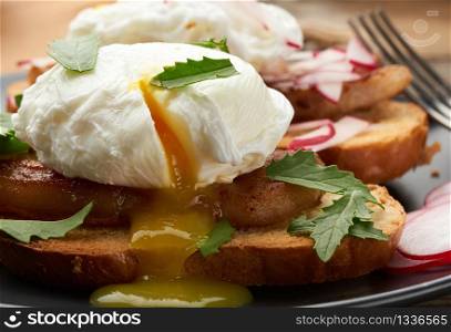sandwich on toasted white slice of bread with poached eggs, green leaves of arugula and radish, morning breakfast on a brown wooden board, close up