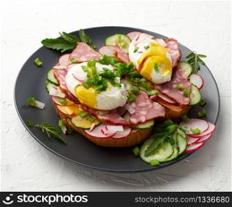 sandwich on toasted white slice of bread with poached eggs, green leaves of arugula, cucumber and radish, morning breakfast on a round plate, white background, eggs benedict