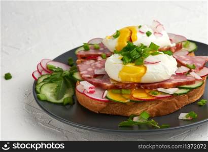 sandwich on toasted white slice of bread with poached eggs, green leaves of arugula, cucumber and radish, morning breakfast on a round plate, white background, eggs benedict