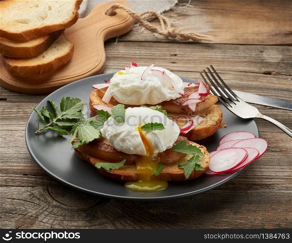 sandwich on toasted white slice of bread with poached eggs, green leaves of arugula and radish, morning breakfast on a gray wooden board, close up