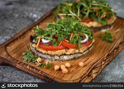Sandwich toasted rustic bread with chickpea hummus, tomato slices, mix of lettuce and microgreens. Vegetarian breakfast.