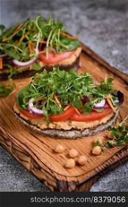  Sandwich toasted rustic bread with chickpea hummus, tomato slices, mix of lettuce and microgreens. Vegetarian breakfast. 