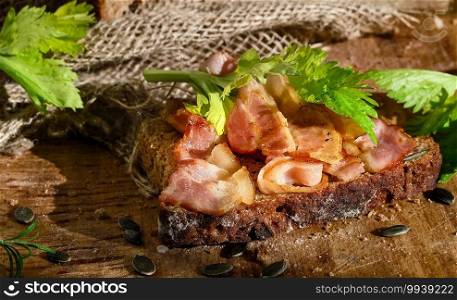 Sandwich with bacon and celery leaves on a slice of rye bread made from leaven with pumpkin seeds. Healthy food concept, traditional craft bread, close-up