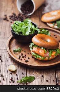 Sandwich with bagel and salmon, cream cheese and wild rocket in bowl and coffee cup with beans on wooden table background