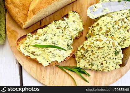 Sandwich with butter from butter, spinach and pickles, a knife, a bowl with butter, cloth, bread and rosemary on a wooden boards background on top