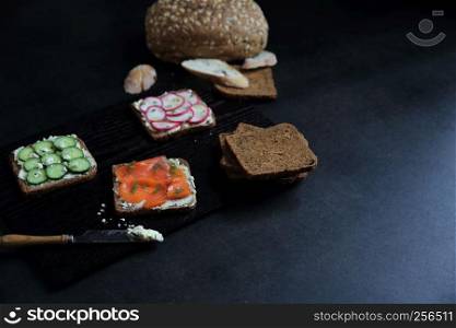 Sandwich with cereals bread smoked salmon beetroot and cucumber on dark marble background