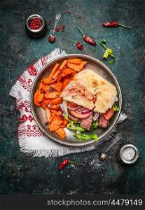 Sandwich with ciabatta bread , roasted meat, vegetables and sweet potato in plate on rustic wooden background, top view