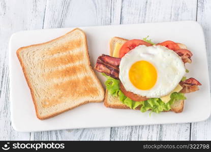 Sandwich with fried egg and bacon on the white plate