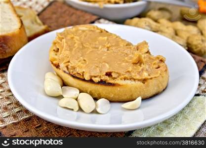 Sandwich with peanut butter in a plate with nuts on a napkin, bread on a wooden boards background