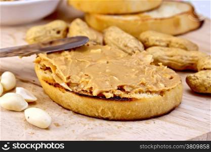 Sandwich with peanut butter, nuts, and a knife on a wooden boards background