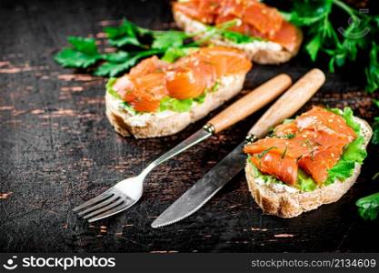 Sandwich with pieces of salmon and greens. Against a dark background. High quality photo. Sandwich with pieces of salmon and greens.