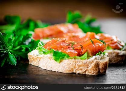 Sandwich with pieces of salmon and greens. Against a dark background. High quality photo. Sandwich with pieces of salmon and greens.