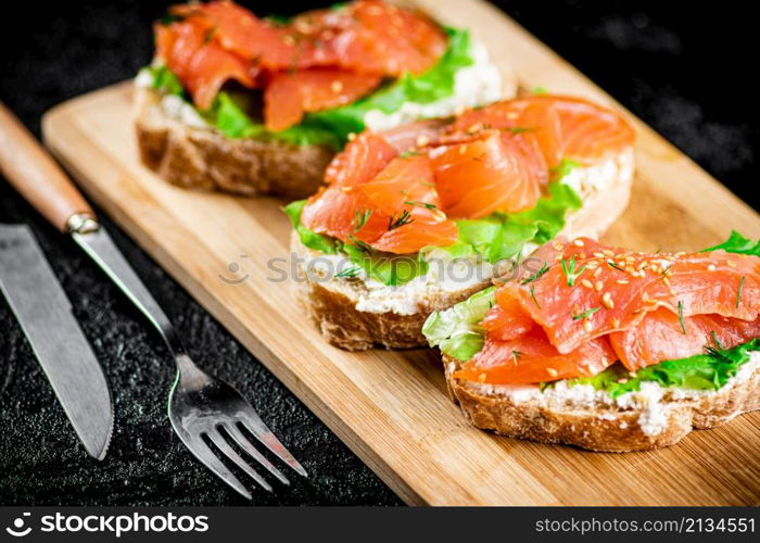 Sandwich with pieces of salmon on a cutting board. On a black background. High quality photo. Sandwich with pieces of salmon on a cutting board.