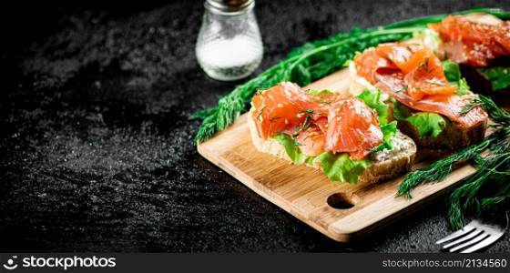 Sandwich with pieces of salmon on a cutting board. On a black background. High quality photo. Sandwich with pieces of salmon on a cutting board.