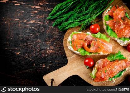 Sandwich with pieces of salmon on a cutting board. On a black background. High quality photo. Sandwich with pieces of salmon on a cutting board.